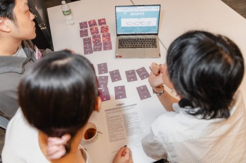 Students huddle around a computer screen with cards describing their resources